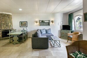 Un salon avec une cheminée en pierre, un canapé, une table à manger et un téléviseur.