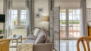 A living room with a sofa, a table, a TV, and a view of the outside.