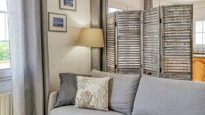 A room with a grey sofa, a lamp, and a view of the outdoors through a window.