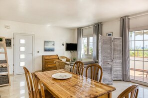 A dining area with a wooden table, chairs, a television, and a view through a window.
