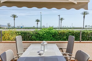 An outdoor seating area with a table and chairs, a clear view of the sea, and palm trees in the background.