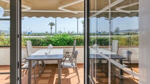 A balcony with a table and chairs, a glass door, and a view of greenery and a distant landscape.