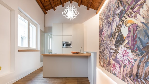A modern kitchen with a central island, a large decorative mural, and a chandelier.