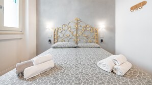 A bedroom with a patterned bedspread, a decorative headboard, and rolled towels on the bed.