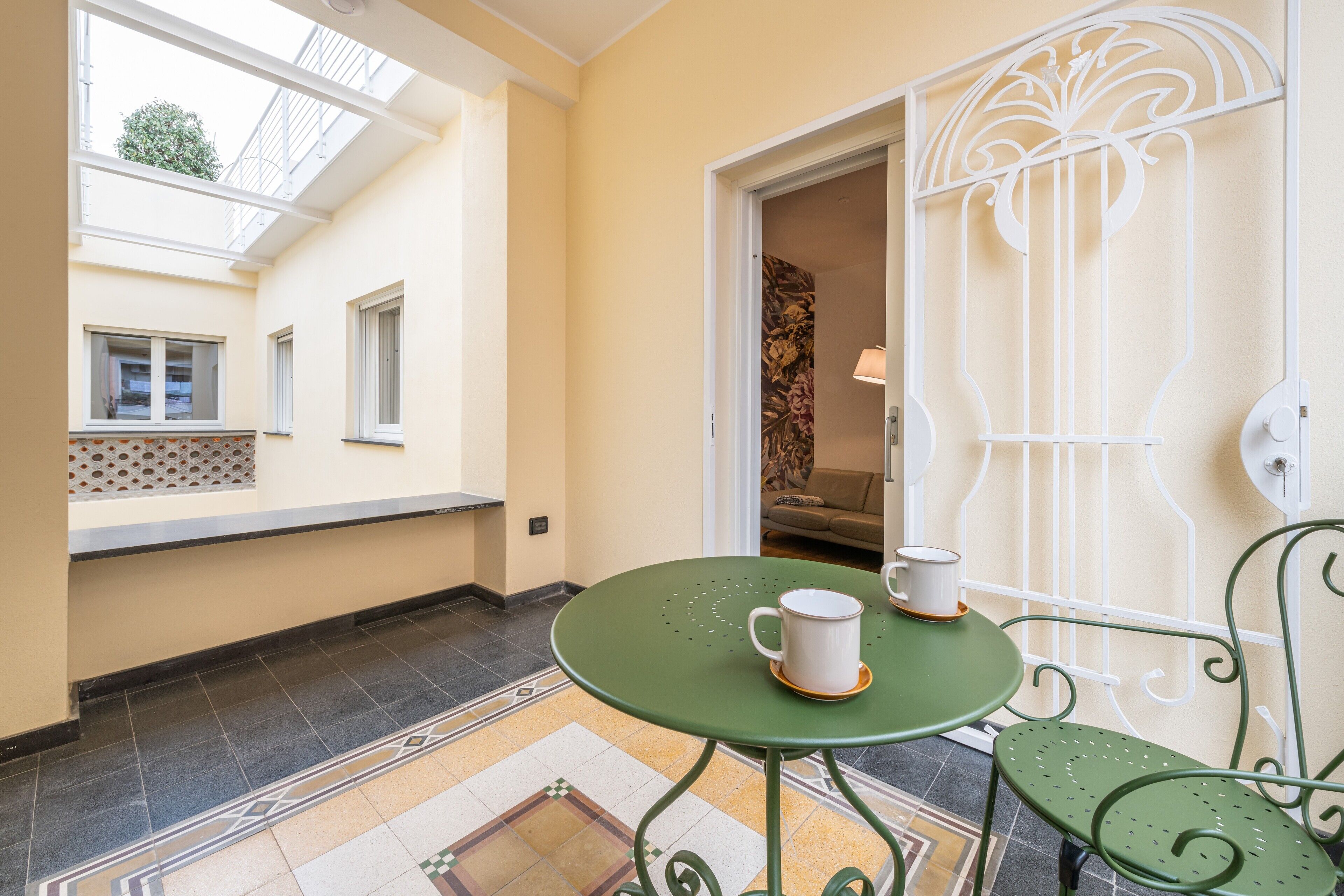 A small room with a green table and chairs, a window, and a door with a decorative metal gate.