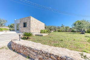 Un edificio de piedra con un pequeño porche, rodeado por un muro de piedra y un área verde con árboles.