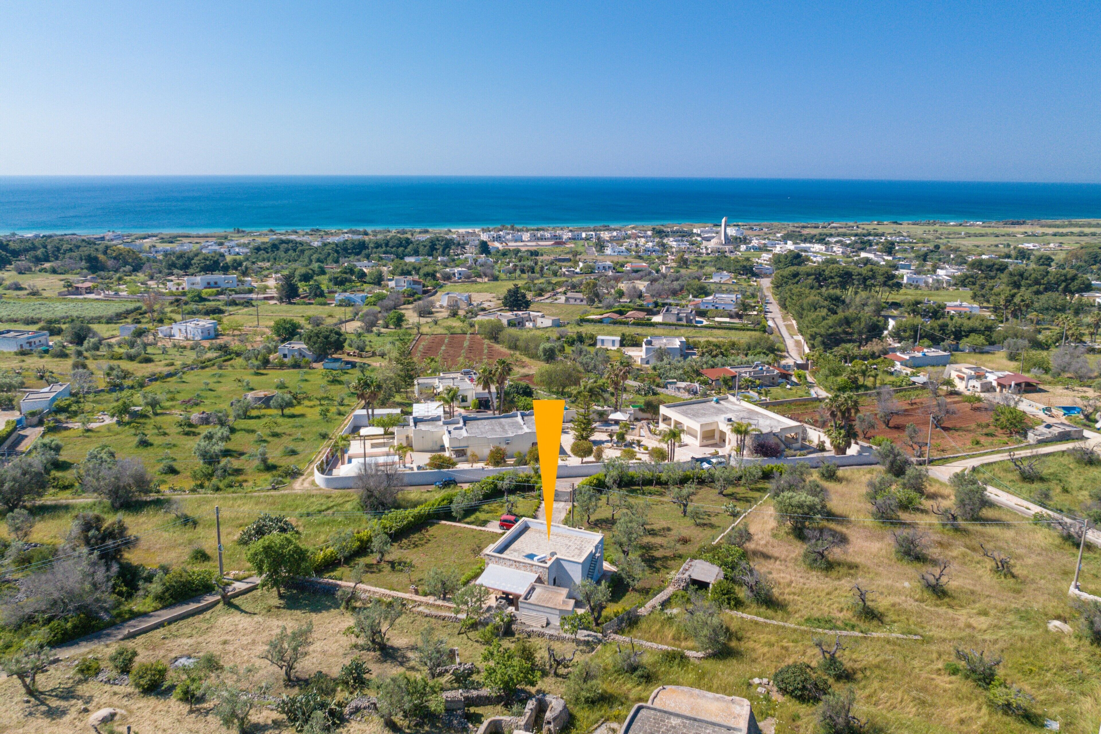 An aerial view of a coastal town with houses, a prominent yellow marker, and the ocean in the background.