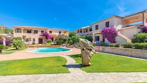 Una piscina rodeada de un césped cuidado, un sendero de piedra y una gran escultura de roca.