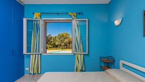 Un dormitorio con cama, ventana con cortinas, mesita de noche y vistas a una piscina y árboles.