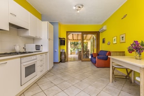 A kitchen with white cabinets, a stove, and a microwave. There is a dining area with a table and chairs, and a sofa.