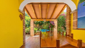 Un patio cubierto con una mesa y sillas de madera, paredes de ladrillo y vistas a follaje.