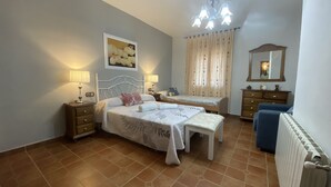 A bedroom with two beds, a nightstand, a dresser, a mirror, a radiator, and a chandelier.