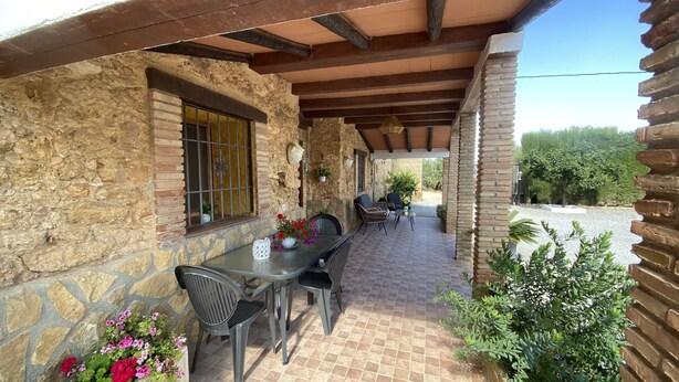 A covered patio with stone walls, a table with chairs, and potted plants.