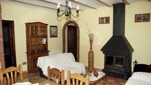 A dining area with a wooden table, chairs, a chandelier, a fireplace, and a checkered sofa. - Holiday Home 'Rural Fábrica Del Azúcar 2' with Mountain View, Wi-Fi and Air Conditioning (Pozo Alcon)