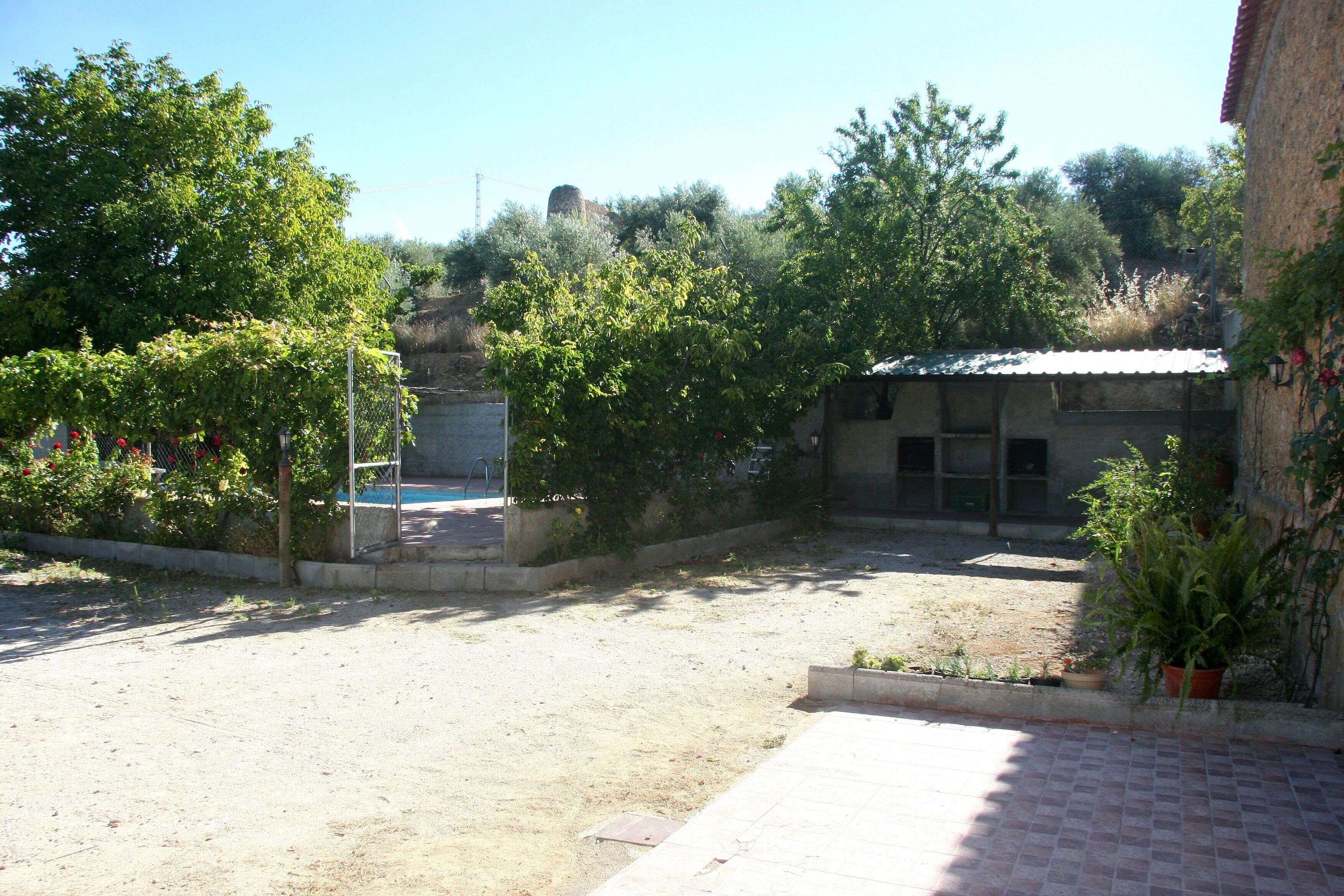 Un patio con piscina, árboles y un edificio de techo con tejas.