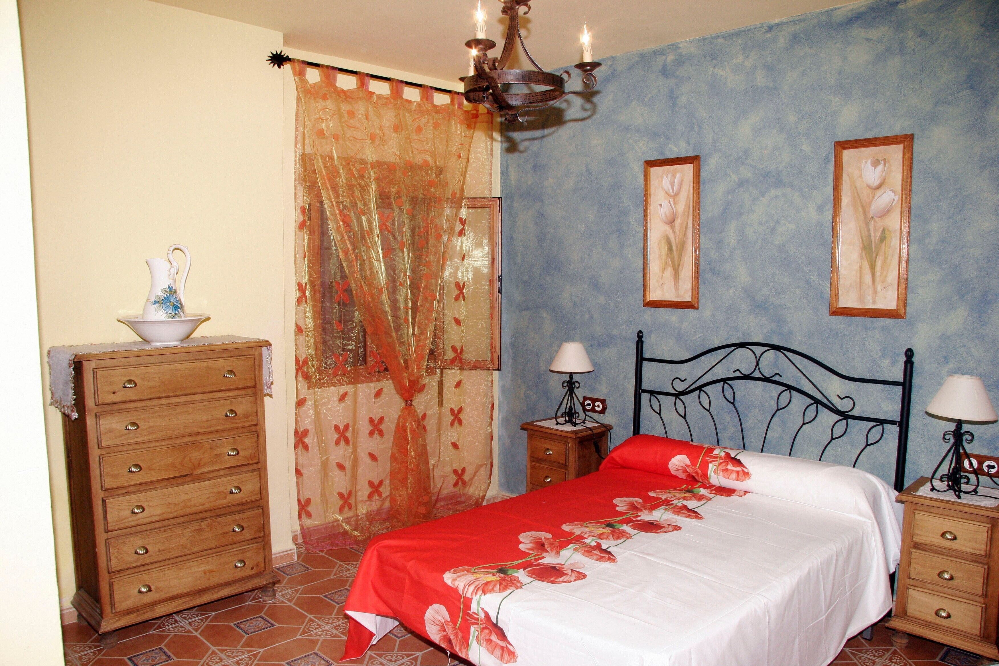 A bedroom with a bed, wooden dresser, nightstands, and a chandelier.