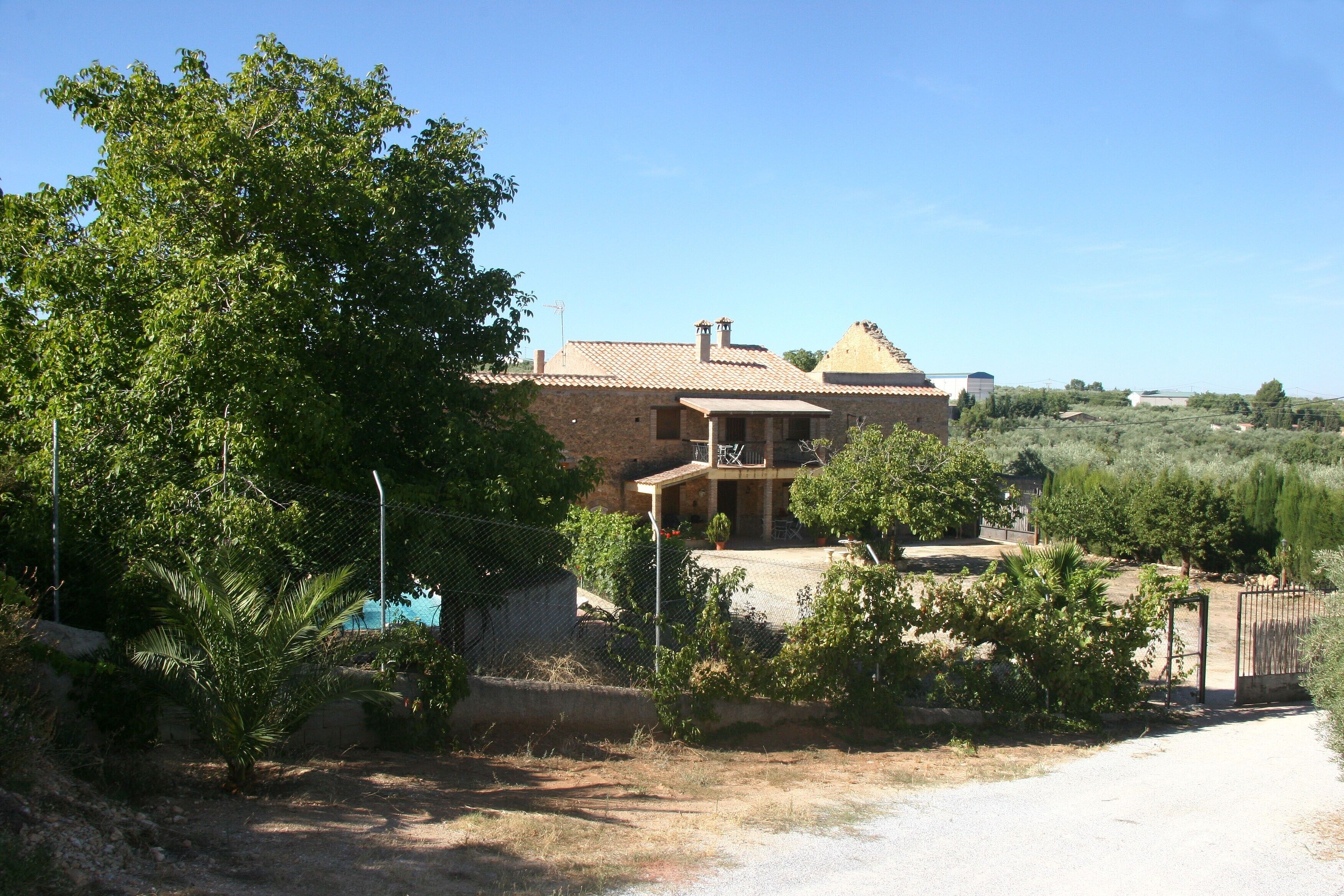 A house with a balcony, surrounded by greenery and a clear sky.