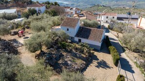 A rural house with a tiled roof, surrounded by olive trees and a gravel path.