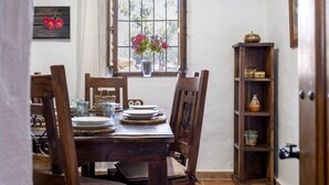 A dining area with a wooden table set for four, a window with a view, and a wooden bookshelf.