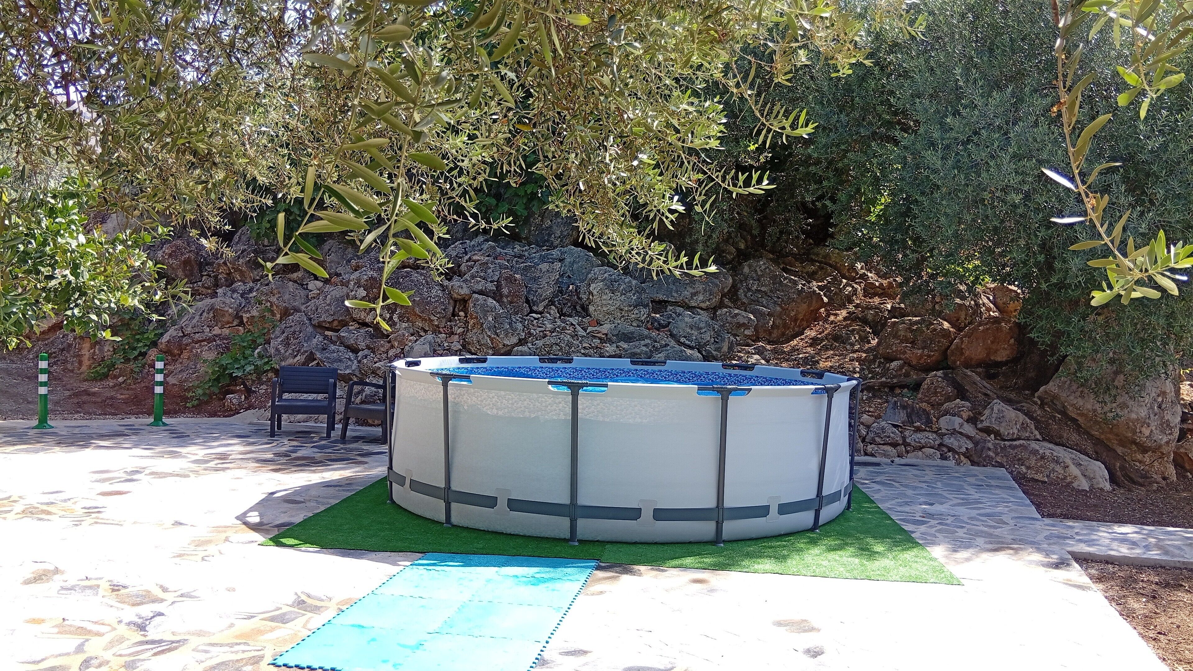 An outdoor hot tub surrounded by rocks and greenery, with a chair and a mat nearby.