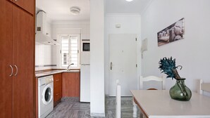 A kitchen with a washing machine, a dining table with chairs, and a vase with a plant.