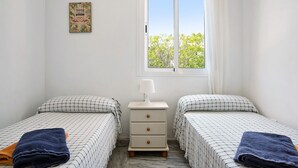A bedroom with two beds, a nightstand, a window with curtains, and a wall-mounted picture.