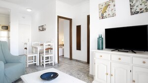 Ein Wohnzimmer mit Fernseher, weißen Möbeln und Bildern an der Wand.