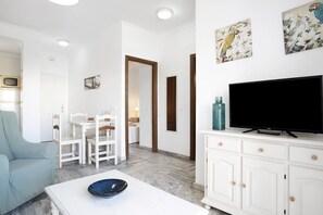 Un salon avec un téléviseur, des meubles blancs et des œuvres d’art accrochées au mur.