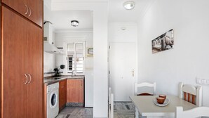 Eine kompakte Küche mit Waschmaschine, ein Essbereich mit Tisch und Stühlen sowie eine weiße Tür zu einem weiteren Zimmer.
