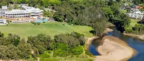 A large, multi-story building with a modern architectural design, surrounded by lush greenery and a river.