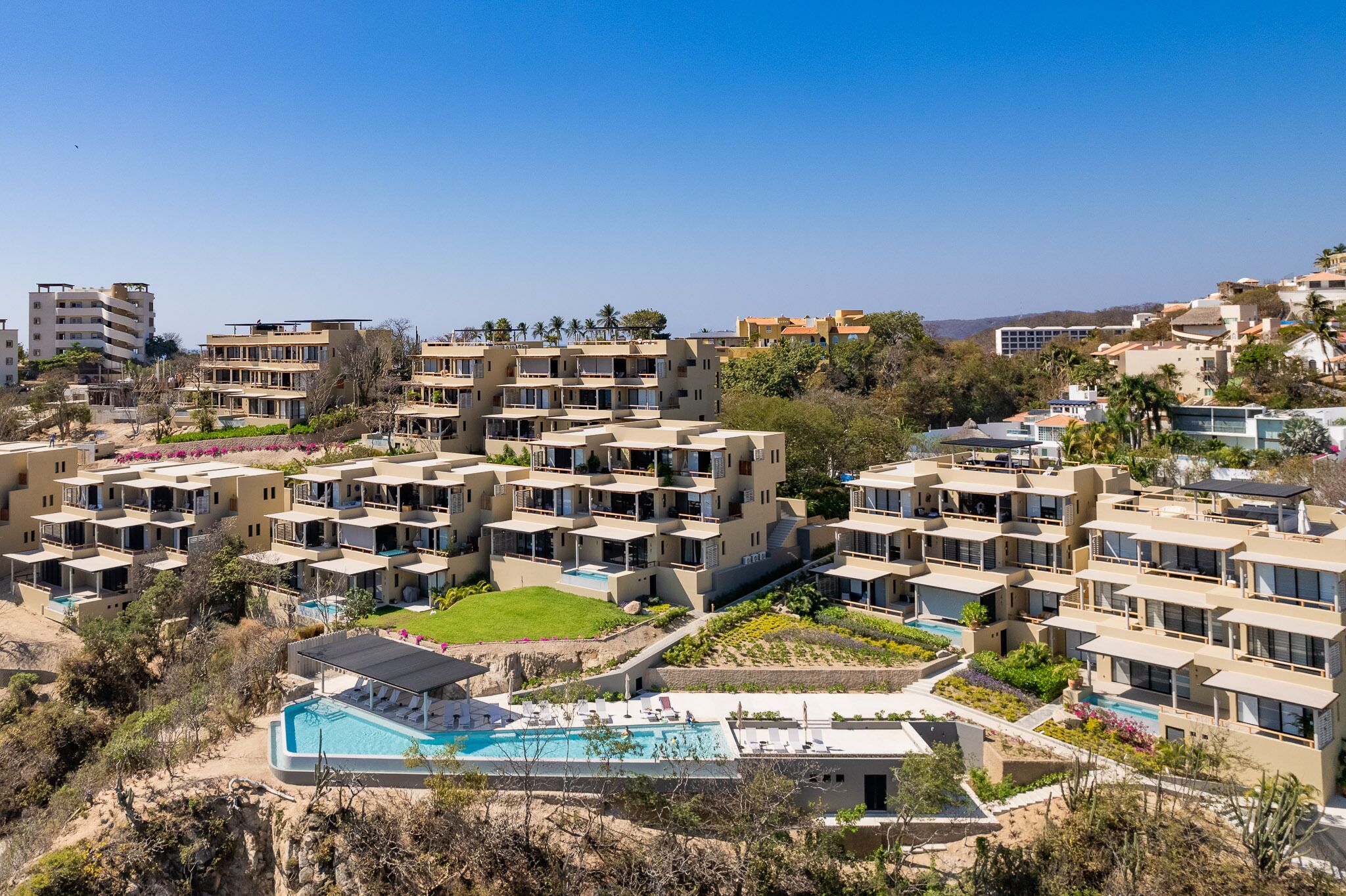A modern hotel complex with multiple buildings, a central swimming pool, and landscaped gardens.