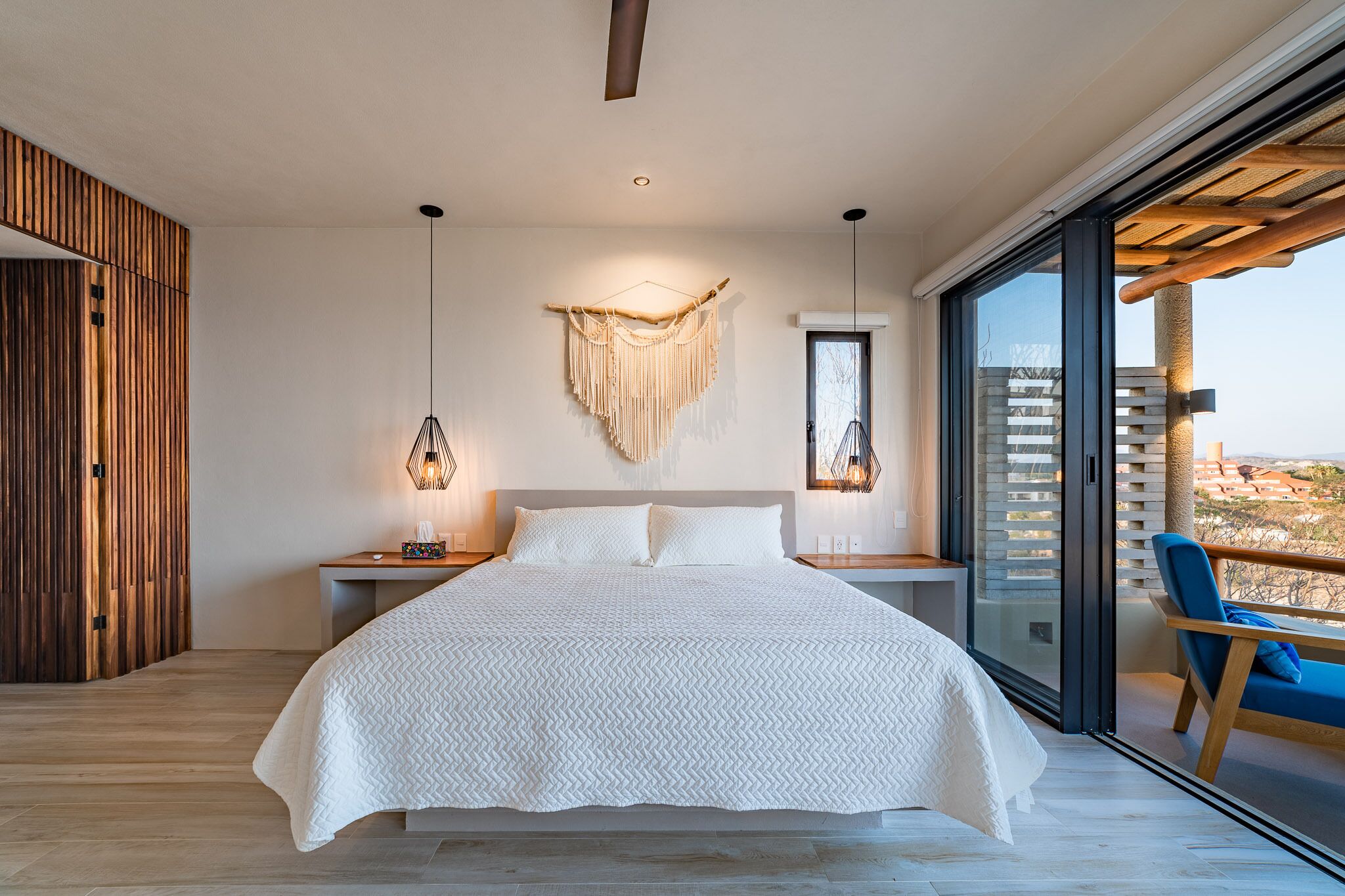 A modern bedroom with a large bed, wooden panel wall, and a balcony with a view.
