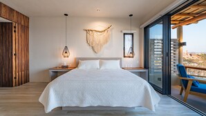 A modern bedroom with a large bed, wooden panel wall, and a balcony with a view. - Penthouse | Views + Beach Access + Rooftop Terrace (Huatulco)