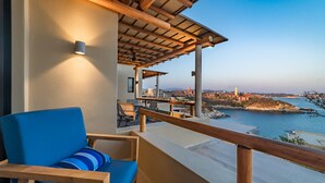 A balcony with a blue chair and wooden railing, overlooking a coastal area with buildings and water. - Penthouse | Views + Beach Access + Rooftop Terrace (Huatulco)