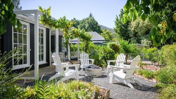 A patio area with Adirondack chairs, a fire pit, and a pergola with vines.
