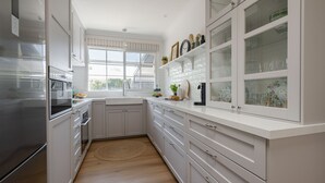 A modern kitchen with white cabinetry, a stainless steel refrigerator, and a window with a view of greenery.