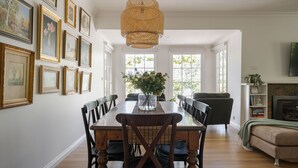 A dining area with a wooden table, chairs, and a vase of flowers. There are framed pictures on the wall and a television on the right.