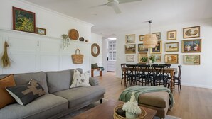 A spacious living room with a grey sofa, dining area with a wooden table and chairs, and a hallway leading to another room.