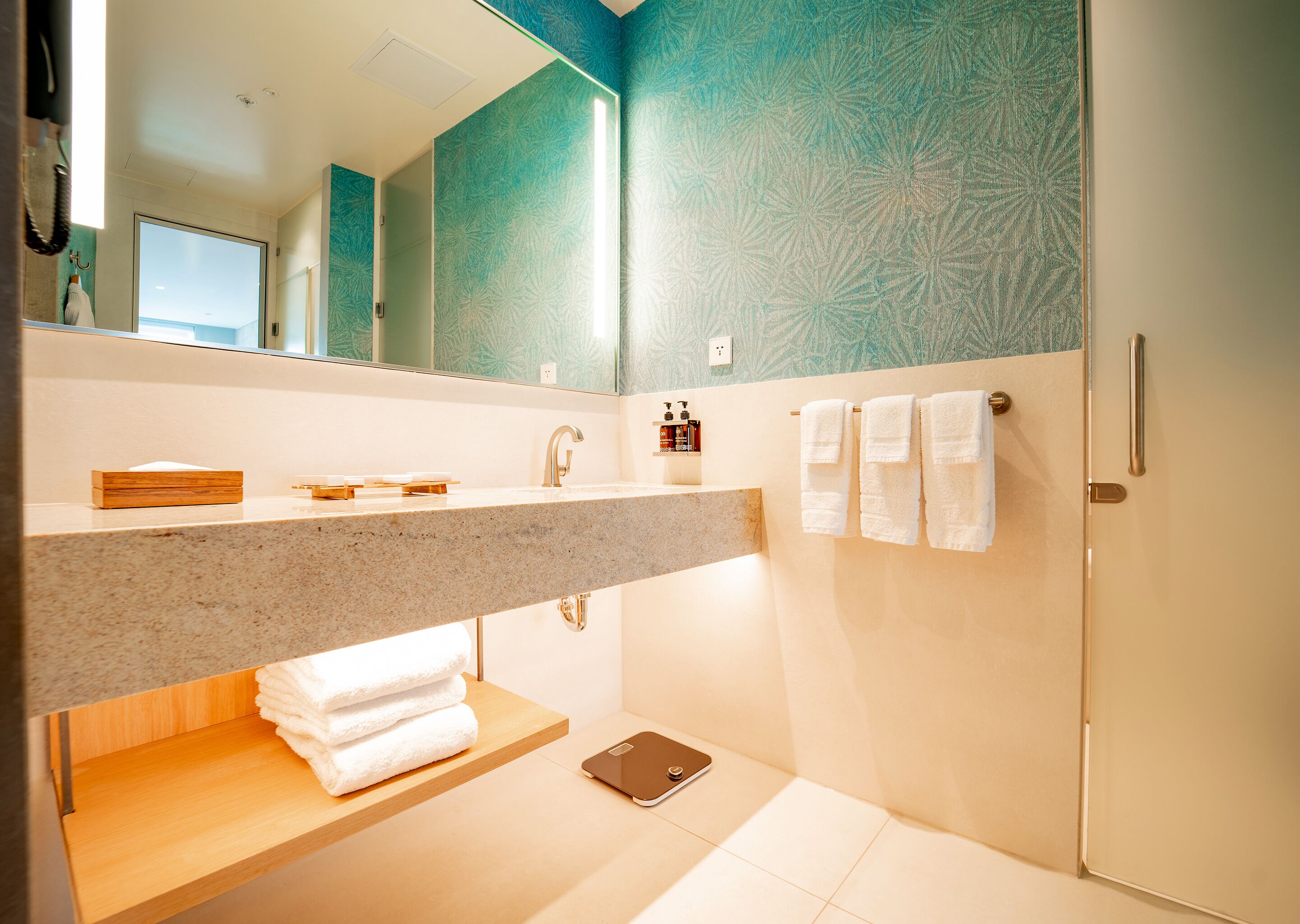 Un baño moderno con encimera de granito, un espejo, toallero y zona de ducha.