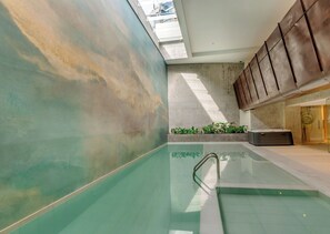 An indoor swimming pool with a clear view of the ceiling and walls, a set of stairs leading to an upper level, and a section of the building's exterior visible through a window.