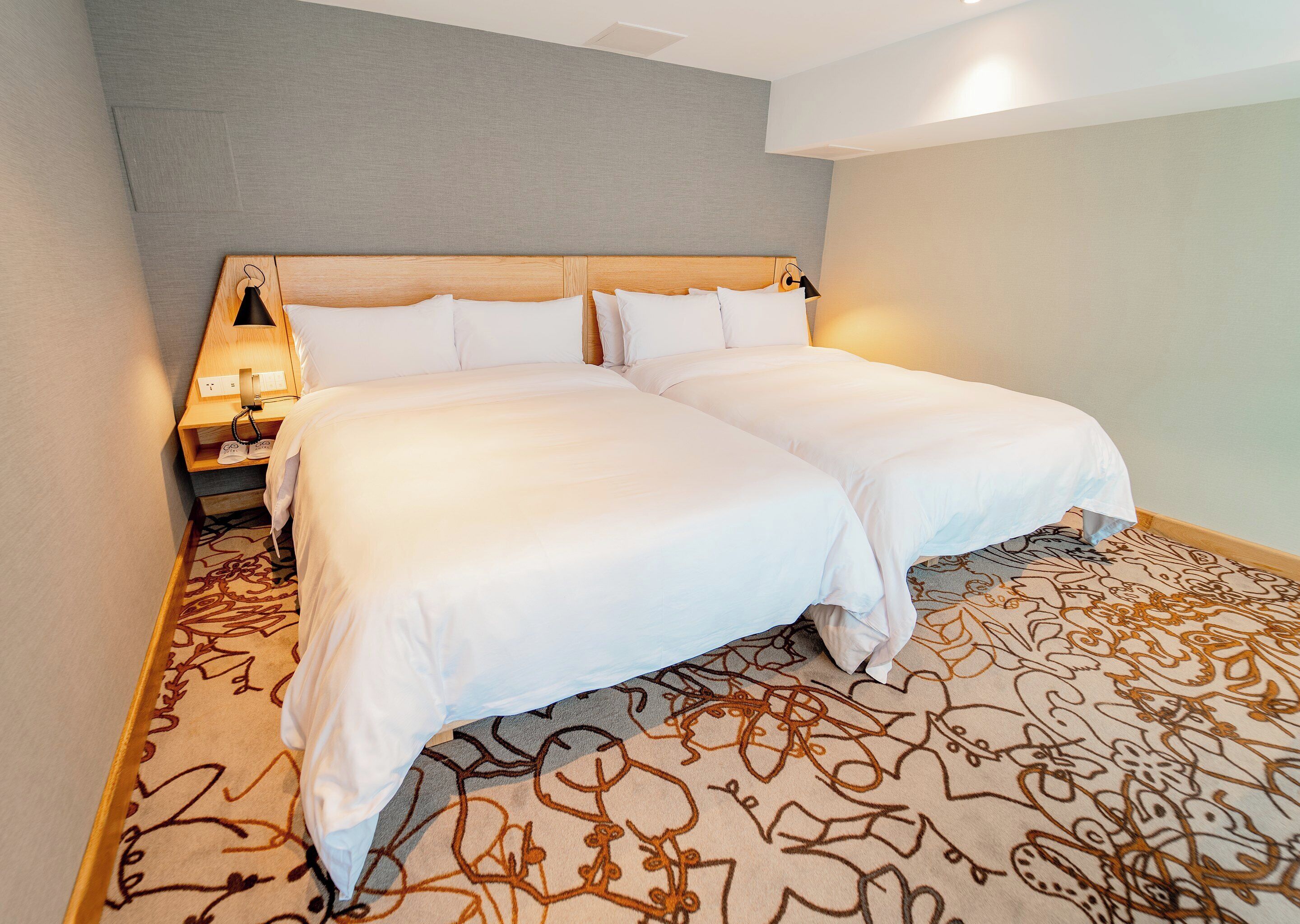 A double bed with white linens, a wooden headboard, and a nightstand with a lamp.