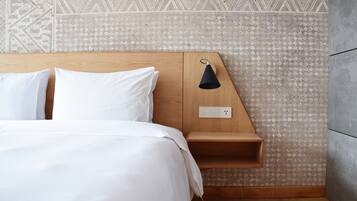 Una cama bien hecha con sábanas blancas, un cabecero de madera, una mesita de noche con lámpara y una pared con diseño.