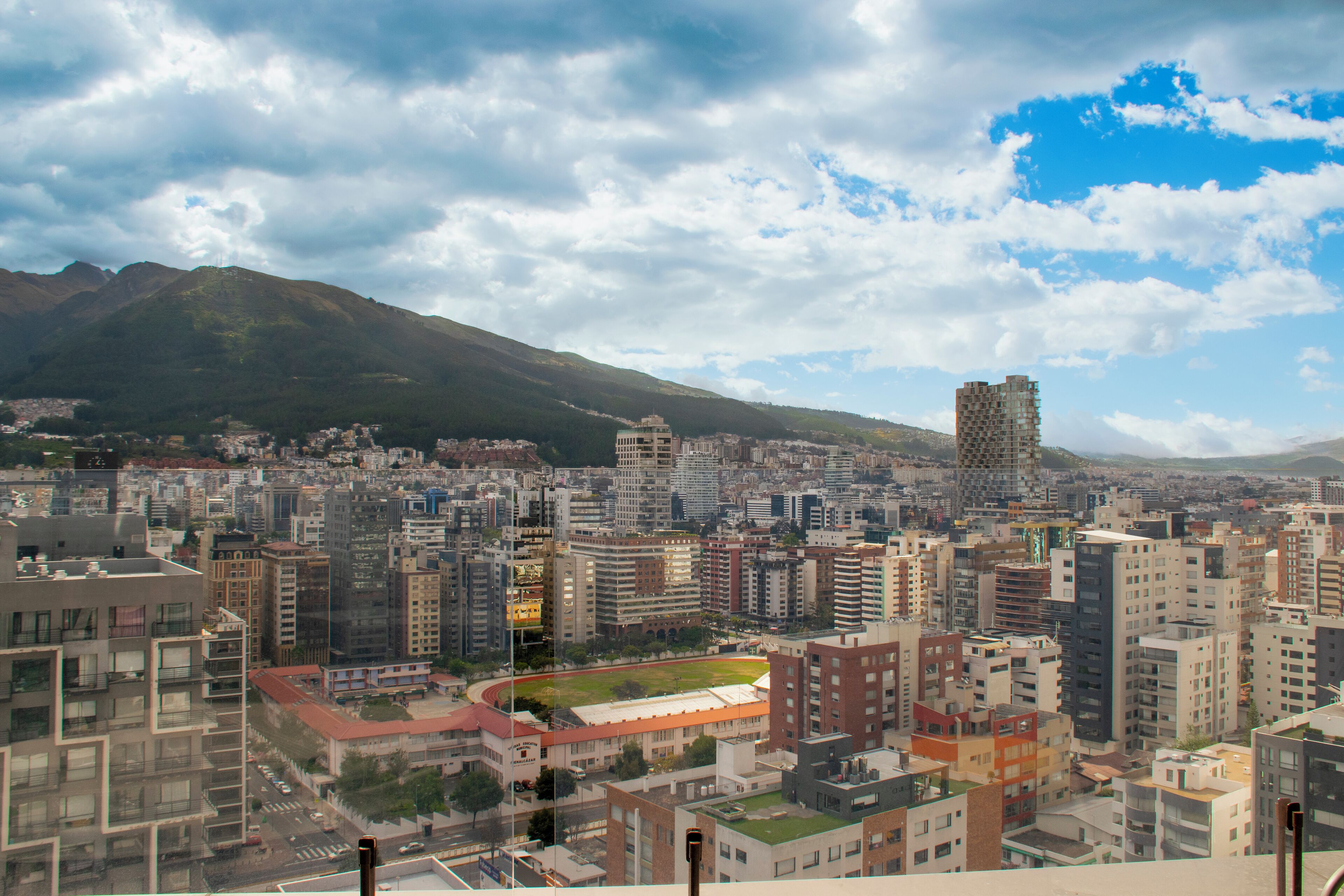 A cityscape with high-rise buildings, a sports field, and a mountain in the background.
