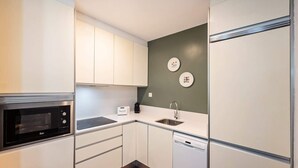 Une cuisine de taille réduite avec des meubles blancs, un micro-ondes noir, un évier et un lave-vaisselle.