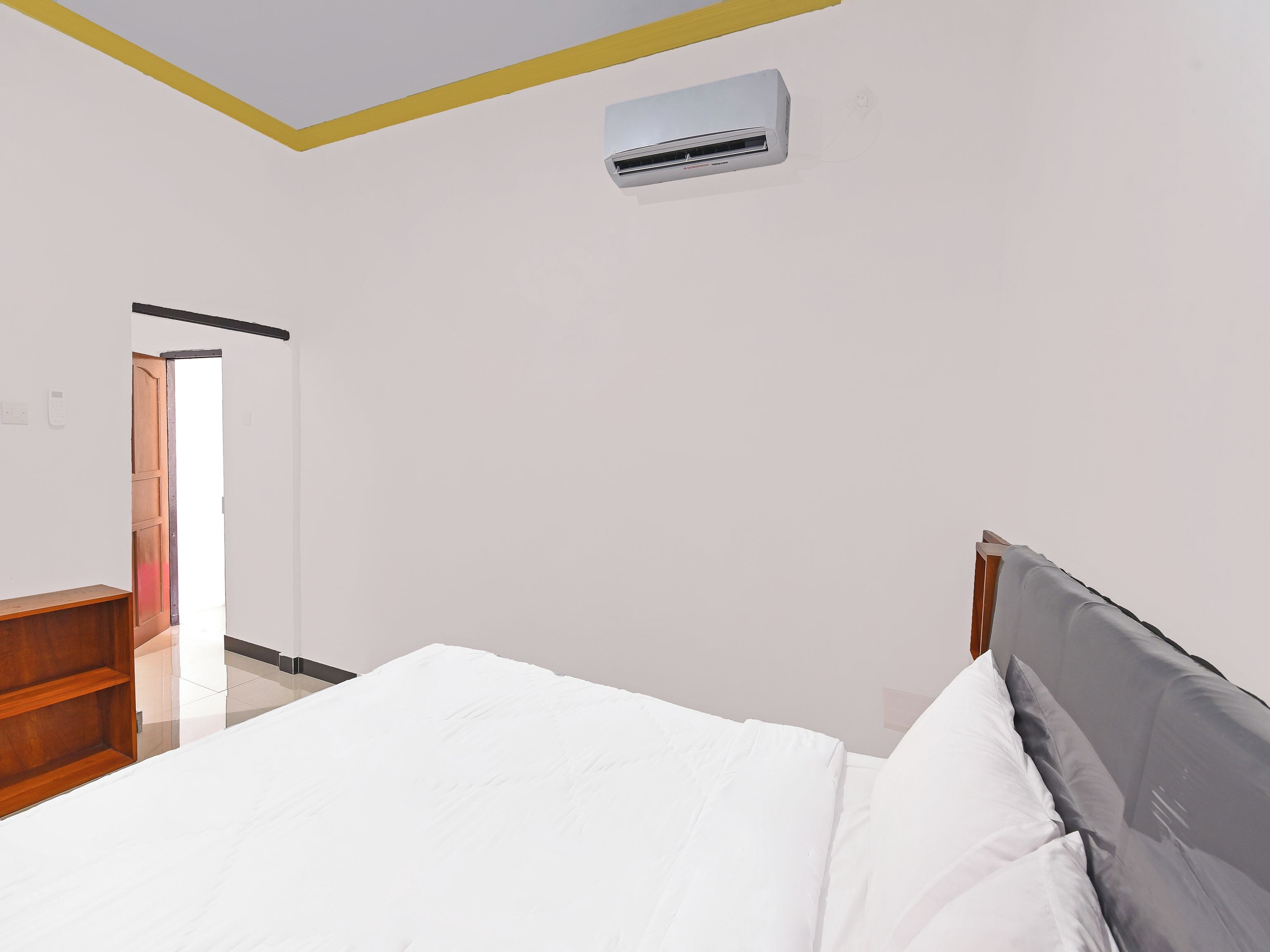 Une chambre à coucher comprenant un lit, une table de chevet en bois, une armoire et un appareil de climatisation fixé au mur.