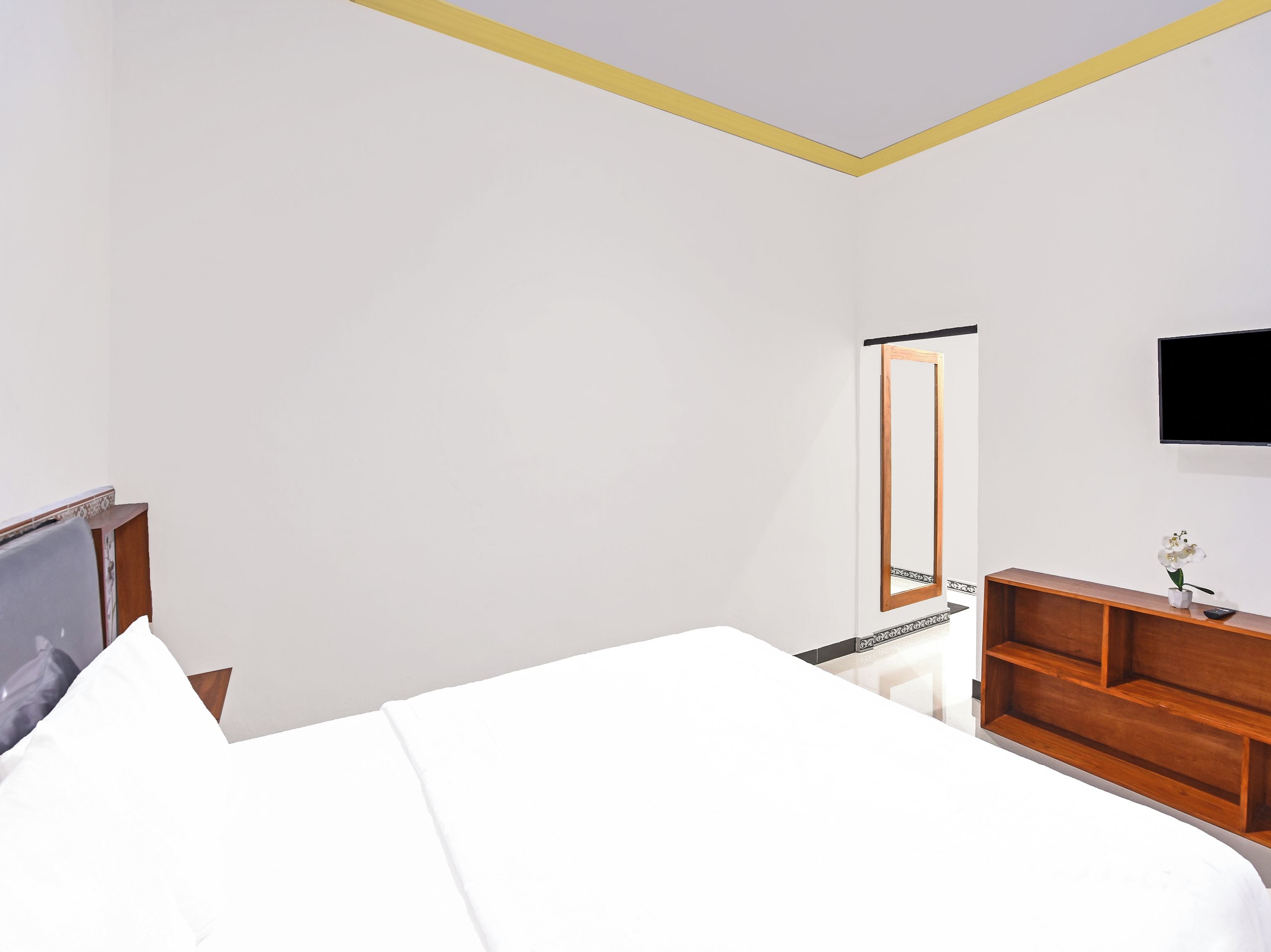 Een hotelkamer met een bed, een houten dressoir, een aan de muur bevestigde televisie en een spiegel.