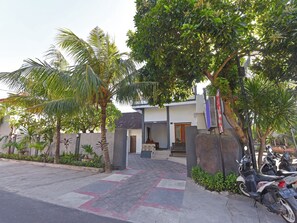 Un edificio moderno con entrada pavimentada, rodeado de palmeras y otra vegetación.