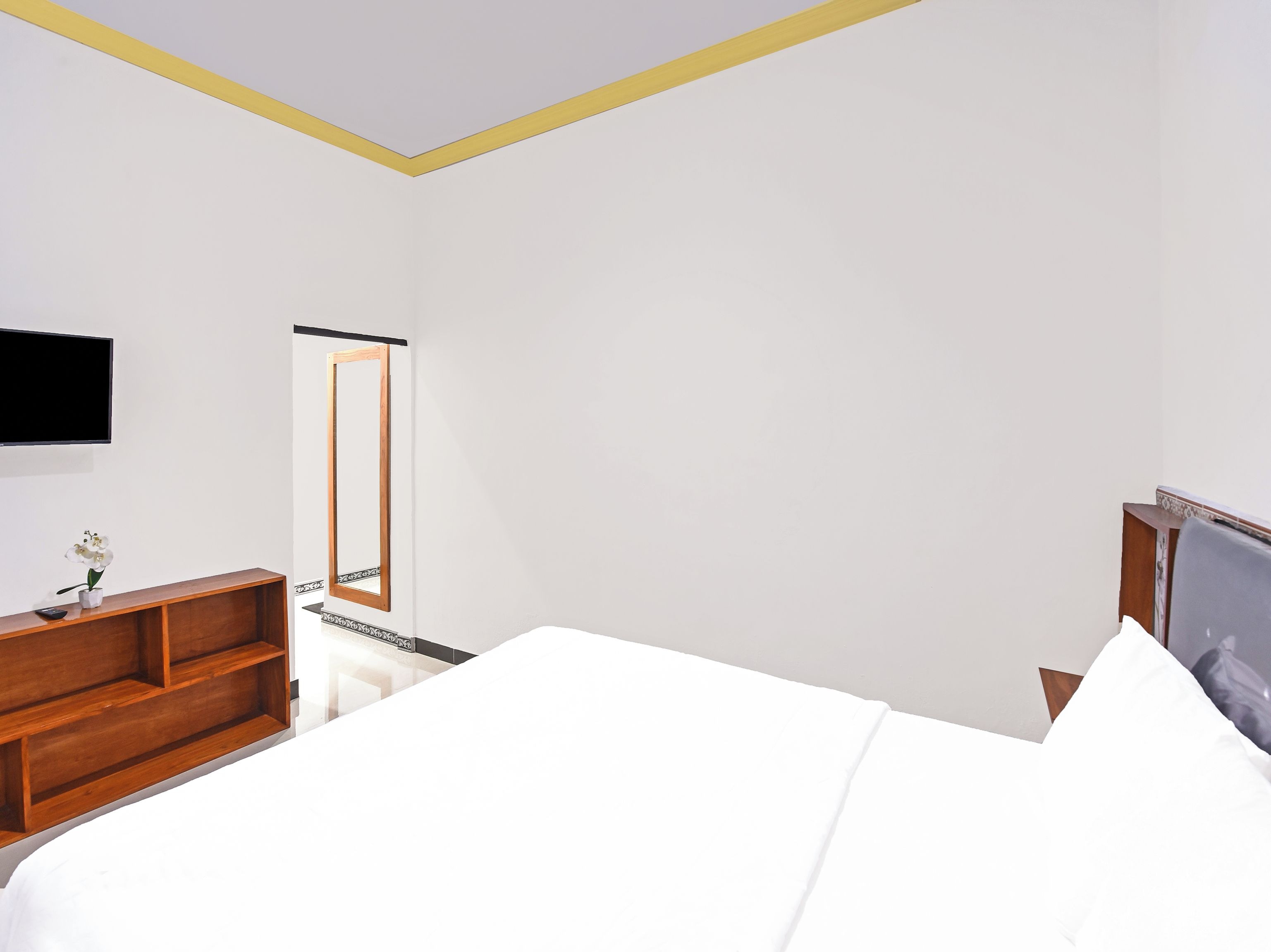 Een hotelkamer met een bed, een houten nachtkastje, een televisie, een spiegel en een kleine tafel met een bloemenvaas.