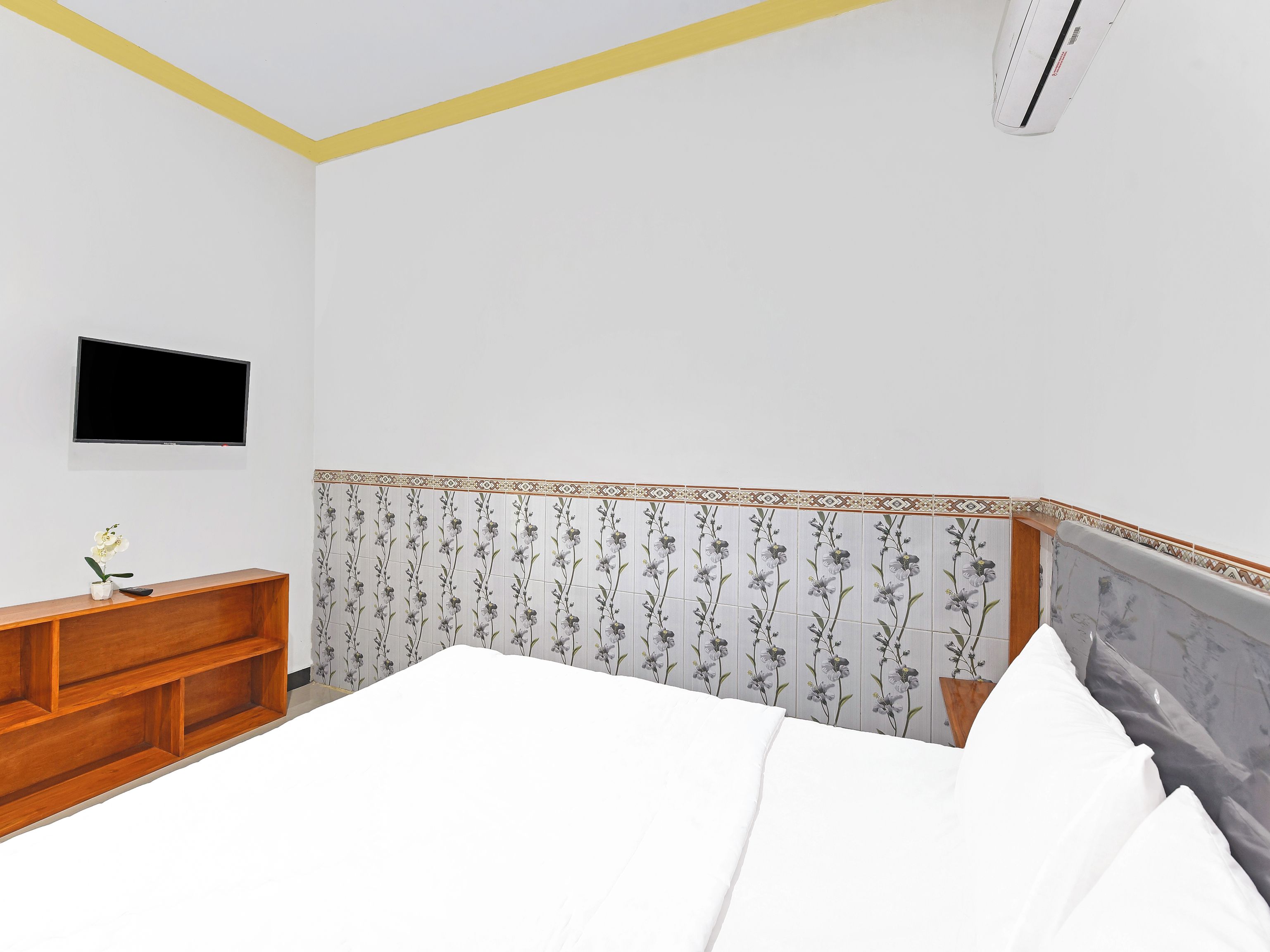 Ein Schlafzimmer mit einem Bett, einem an der Wand montierten Fernseher, einem Holznachttisch und einem dekorativen Kopfteil.