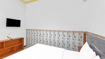 Ein Schlafzimmer mit einem Bett, einem an der Wand montierten Fernseher, einem Holznachttisch und einem dekorativen Kopfteil.